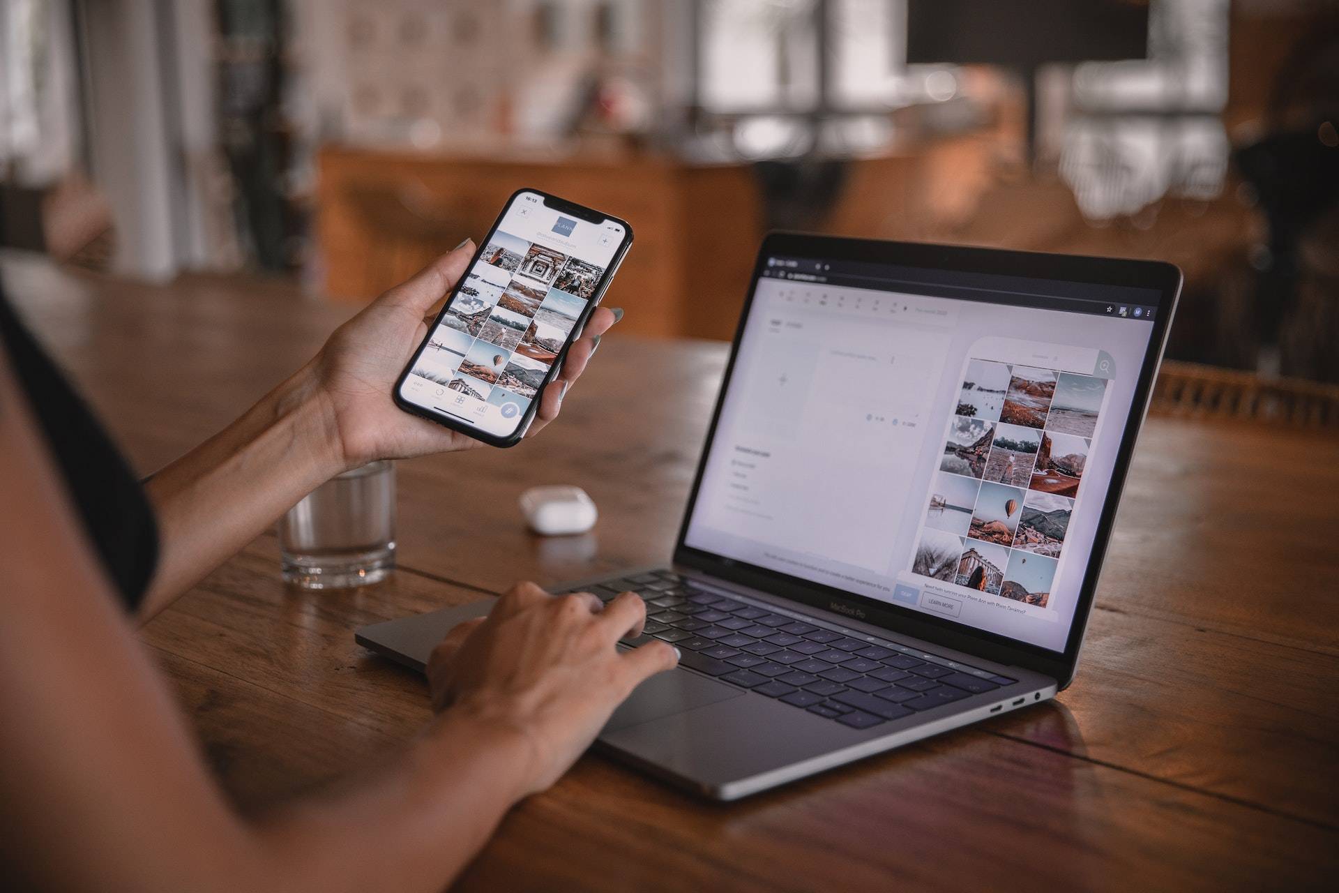 A woman multitasking with a phone and laptop on a wooden table, while working on development projects with the help of AWS and Webflow.